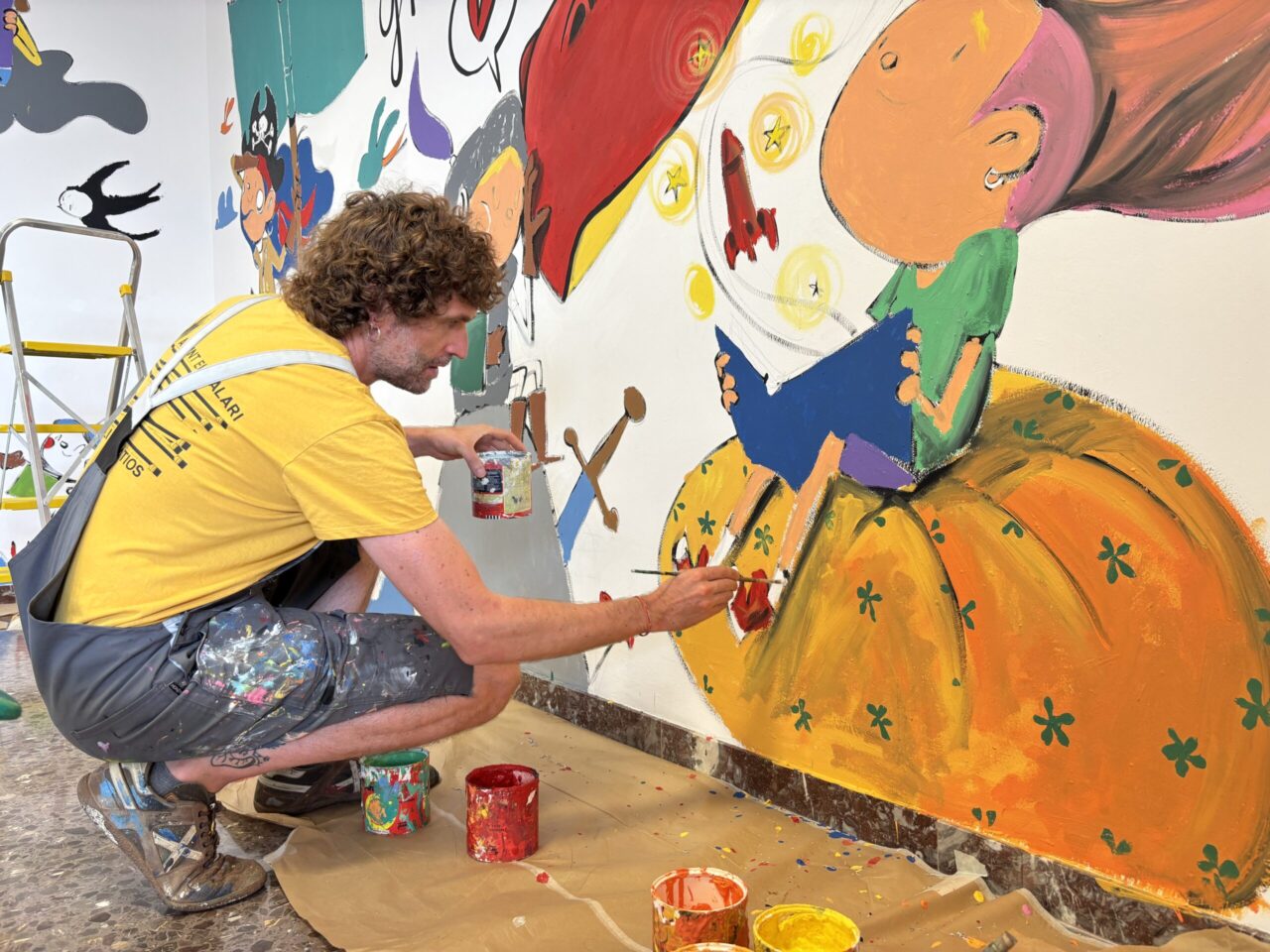 Artista pintant un mural acolorit amb personatges infantils.