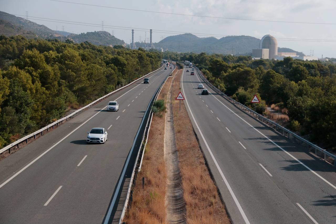 Autopista amb cotxes i una central nuclear al fons.